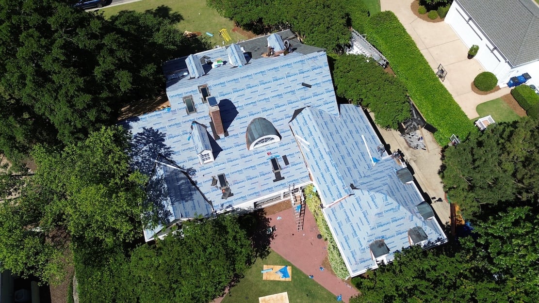 Aerial view of a roof during installation with blue synthetic underlayment.
