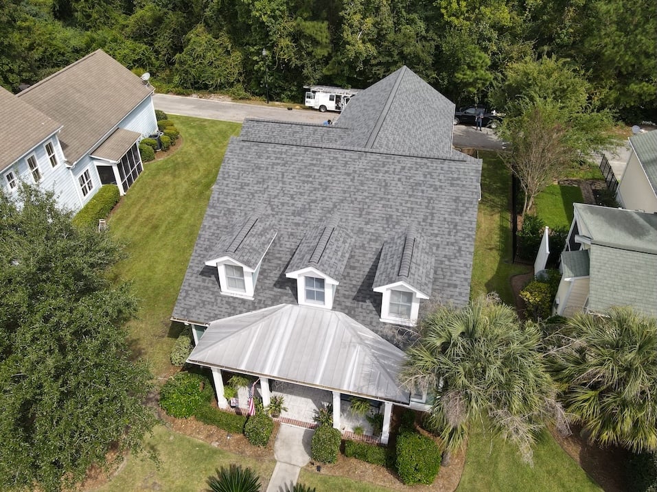 Aerial view of a suburban home featuring a new architectural shingle roof and metal porch roof.